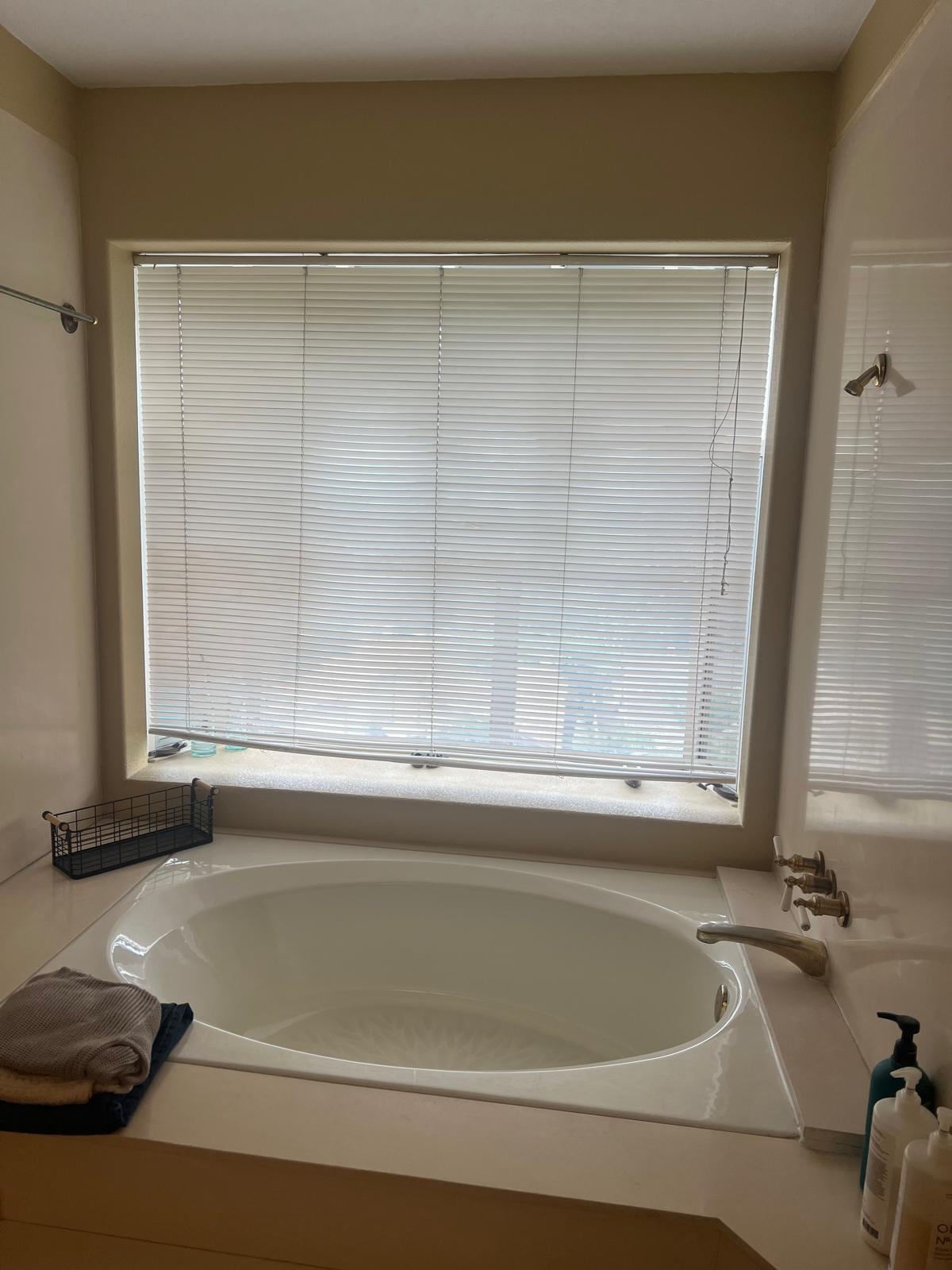 Before: corner oval tub with mini-blinds in a Mission Viejo primary bathroom
